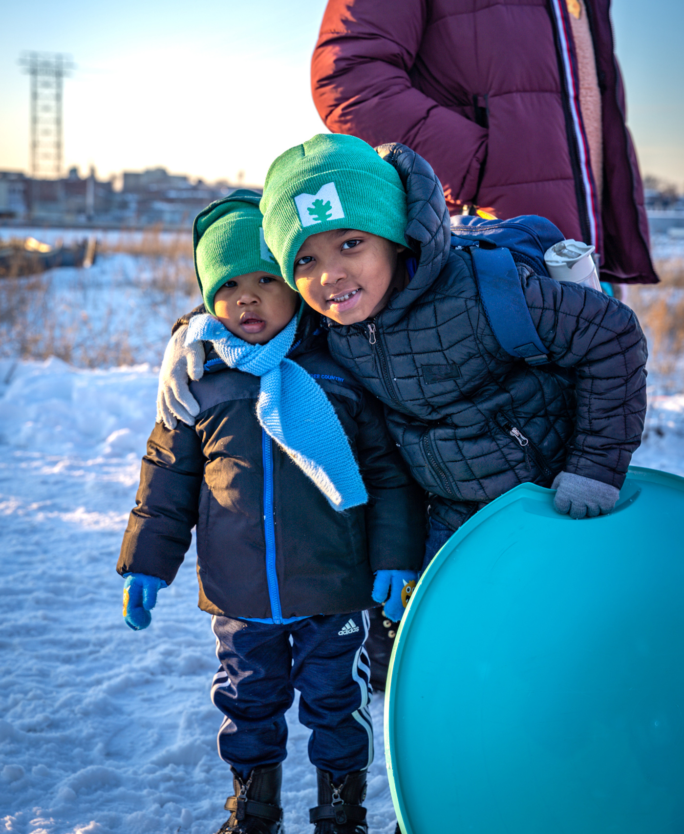 Two little boys posing together for a photo in the snow while holding their sled