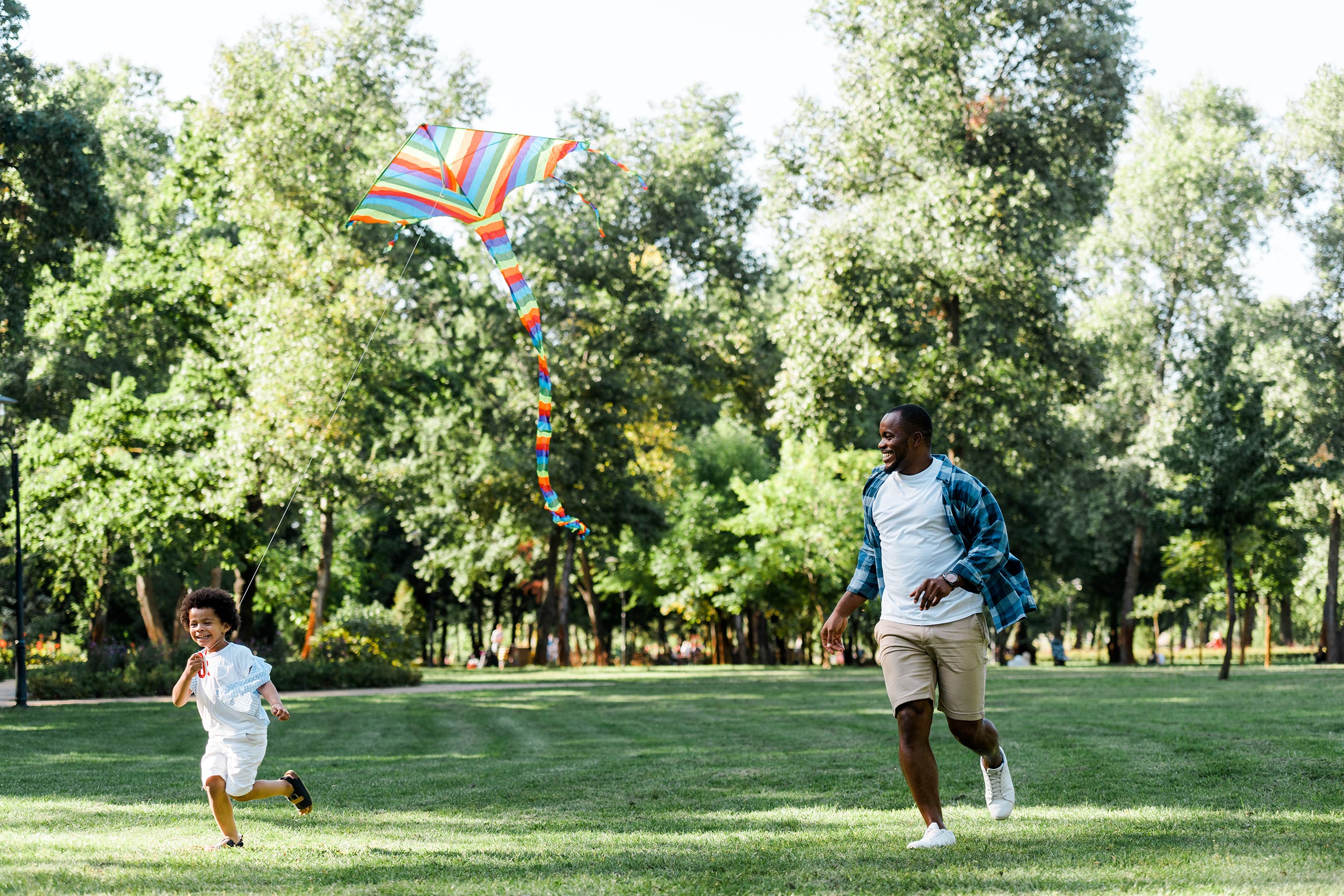 Father and son playing in a green field surrounded by trees with a kite